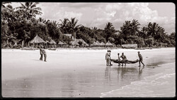 Multiple figures launching a wooden boat into shallow ocean waters with palm-lined beach village visible in background.