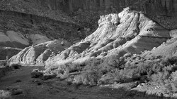 Eroded mineral deposits with distinctive layered formations and sparse desert vegetation in black and white.