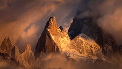 Dramatic mountain peaks bathed in golden light emerge from swirling clouds and mist.