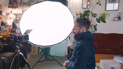 Photographer positioned beside large circular softbox reflector mounted on tripod during studio session.