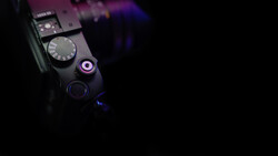 Close-up of a camera's top plate showing mode dial, shutter button, and illuminated control elements against a dark background.