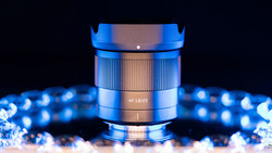 Close-up of a blue and bronze lens with AF 1.8/23 marking, surrounded by bokeh lights on dark background.