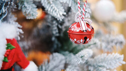 Red decorative jingle bell hanging from a candy cane striped ribbon on a frost-covered evergreen branch.