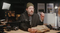 Photographer in studio holding camera gear while discussing equipment setup and techniques.