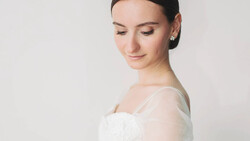 Woman in white off-shoulder dress photographed in profile against neutral background.