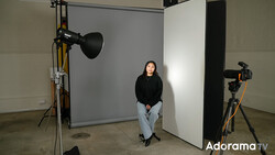Portrait subject seated in professional studio setup with key light and fill reflectors.