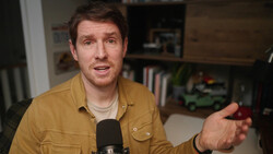 Man in mustard shirt speaking into microphone during interview or podcast recording.
