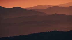 Layered mountain ridges silhouetted against an orange and amber sunset sky.
