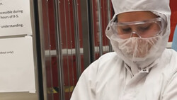 Person wearing full white protective gear including hood, face shield, and goggles in an indoor setting.