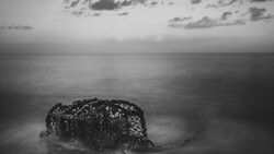 Weathered lobster trap partially submerged in shallow ocean water under overcast sky.