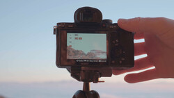 Camera mounted on tripod displaying landscape preview on rear screen during golden hour.