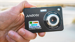 Hand holding a compact Andoer digital camera with 18 megapixel sensor and 1/7-45mm f3.6 lens.