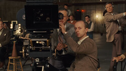 Film director operating a large format movie camera on set with crew members surrounding.