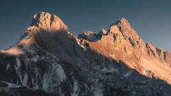 Snow-covered mountain peaks illuminated by warm golden light against a clear blue sky.