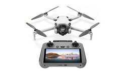 Compact drone with four propellers positioned above its remote controller displaying a landscape photograph on screen.