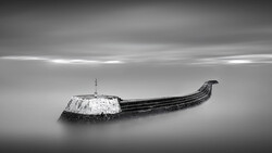 Abandoned wooden boat with snow-covered hull half-submerged in still water.