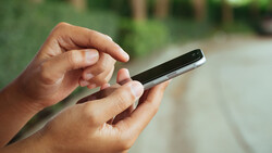 Hands holding a smartphone outdoors with natural daylight illumination.