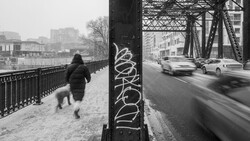 Pedestrian jogging on snowy bridge while cars blur past on adjacent roadway.