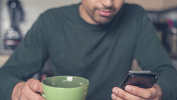 Man holding green cup and smartphone while looking at phone screen.