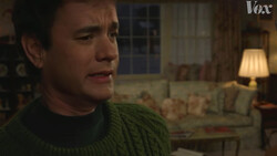 Screenshot from a film showing a man in a green sweater in a warmly lit living room interior.