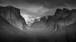 Yosemite Valley shrouded in mist with granite cliffs, forested slopes, and a distant waterfall.