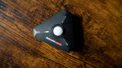 Black triangular camera accessory with white circular button on wooden surface.