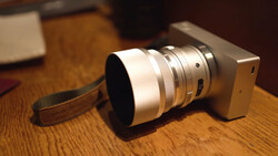 Compact camera with telephoto lens and wrist strap on wooden surface.