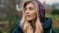 Woman wearing a dark jacket and red plaid hood, photographed outdoors during overcast daylight.