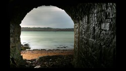 Seascape framed through a stone tunnel opening, showing turquoise water and distant shoreline.