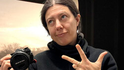 Photographer holding a compact camera while gesturing during discussion or demonstration.