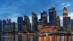 Illuminated skyscraper cityscape at dusk reflected in calm waterfront.
