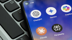 Screenshot showing AI assistant app icons including ChatGPT, Gemini, Copilot, Claude, and Perplexity on a smartphone screen next to a laptop keyboard.