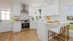 Bright, modern white kitchen with wood flooring, stainless steel appliances, and an island with seating.