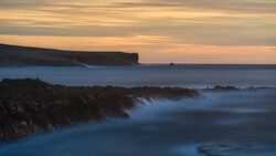 Coastal cliffs and rocky shoreline at twilight with long exposure blur on calm sea.