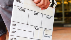 Film production clapperboard held in someone's hands, showing blank fields for title, scene, cut, take, director, and other production details.