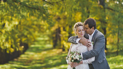 Groom embracing bride from behind in tree-lined garden setting during golden hour.
