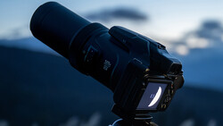 Professional DSLR camera with telephoto lens mounted on tripod against blurred mountain landscape.