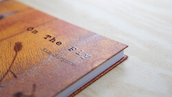 Leather-bound book with embossed title and botanical imagery on cover, photographed at an angle on white surface.