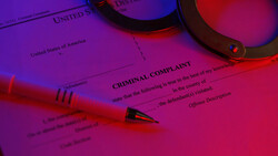 Criminal complaint form illuminated by pink and purple neon lights with glasses and pen.