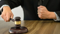 Judge in dark robes striking a gavel on its wooden base during a court proceeding.