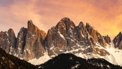Snow-capped mountain peaks with jagged rock formations glowing in golden sunset light.