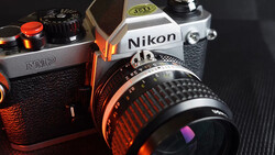 Two vintage film SLR cameras with manual focus lenses displayed on dark textured surface with warm orange lighting.