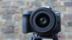 DSLR camera with wide-angle lens mounted on tripod head, shot against blurred urban brick building background.