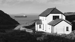White house with dark roof perched on coastal cliffs overlooking the sea, rendered in black and white.