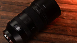 Black telephoto lens with focus ring and aperture markings displayed on warm wooden surface.
