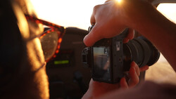 Photographer holding a compact camera while shooting golden hour sunlight through eyeglasses.