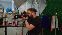 Bearded videographer operating a cinema camera in a studio with professional lighting setup.
