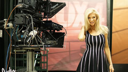 Woman in striped black and white dress posing beside professional cinema camera on set.