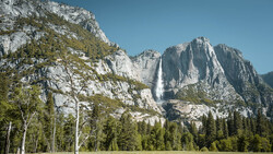 Yosemite Valley with a tall waterfall cascading down granite cliffs surrounded by coniferous forest.