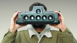 Photographer holding a panoramic film camera with six lenses across its front.